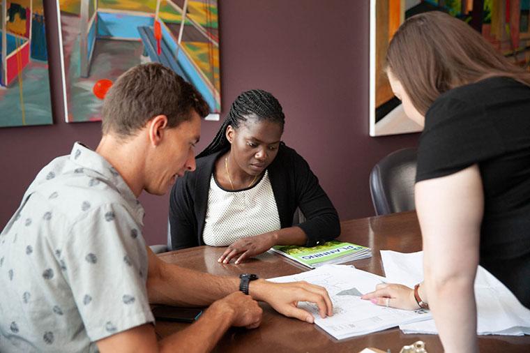 Three students look down at papers on a table