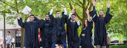 6 graduating students in official University of Guelph academic gowns are jumping in the air