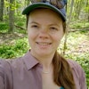 Rosemary with ballcap on stands with trees and forest floor behind her