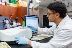 male student wearing a lab coat collecting a sample in a lab.