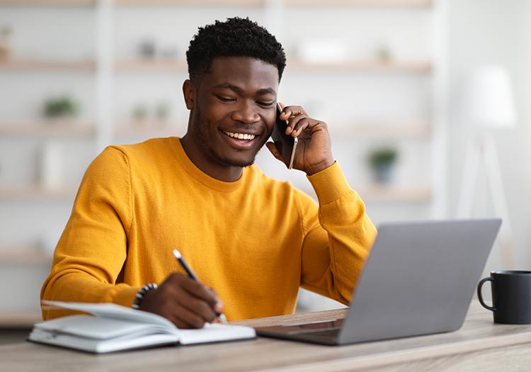 Student on phone in front of laptop with notebook