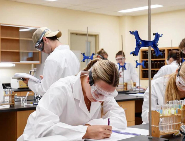 Group of students in Chem1040 lab wearing persona protective equipment and writing in notebooks.