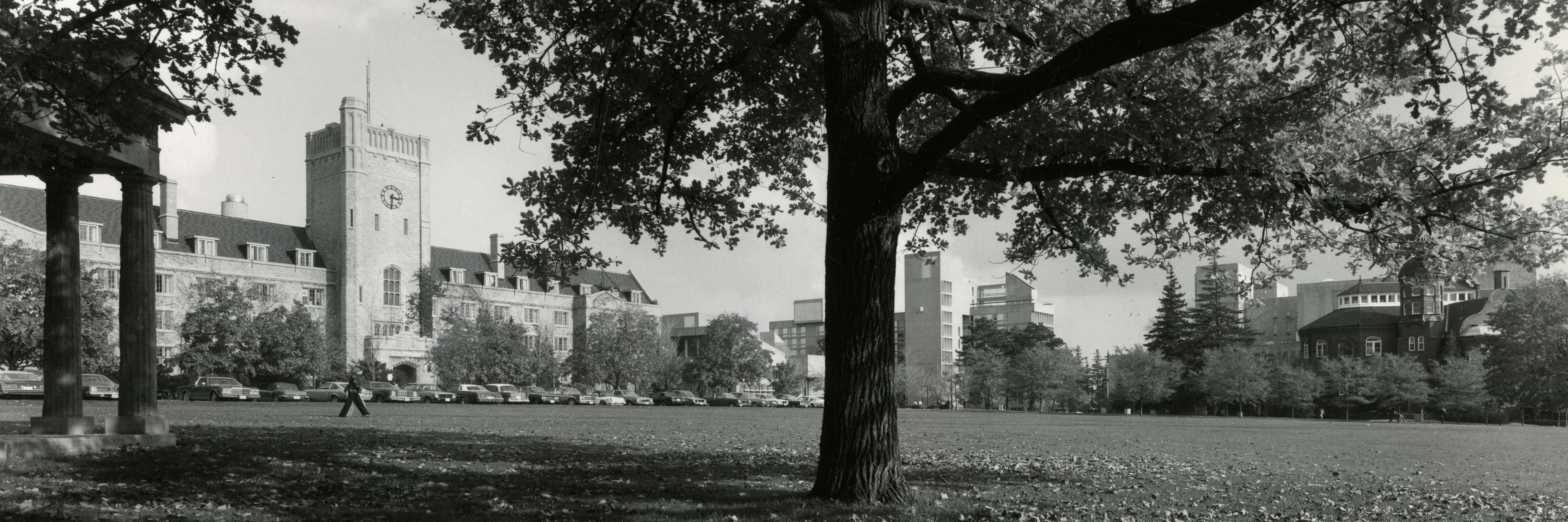 A black and white photo of a stone clock tower building surrounded by a grassy field and trees.