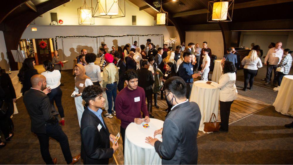 a party with people standing around multiple tables, having conversations