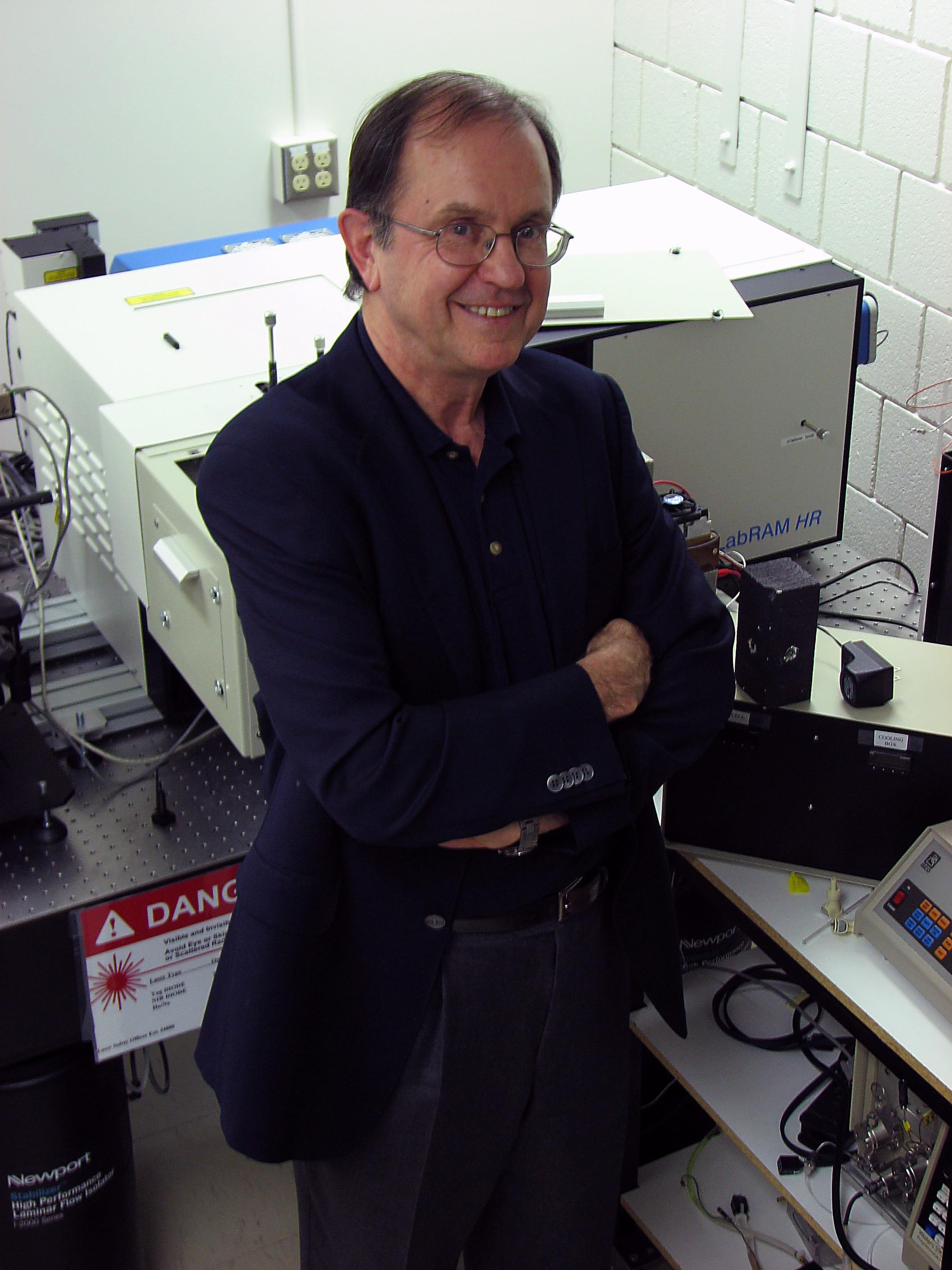 Peter Tremaine stands infront of an instrument with his arms crossed.