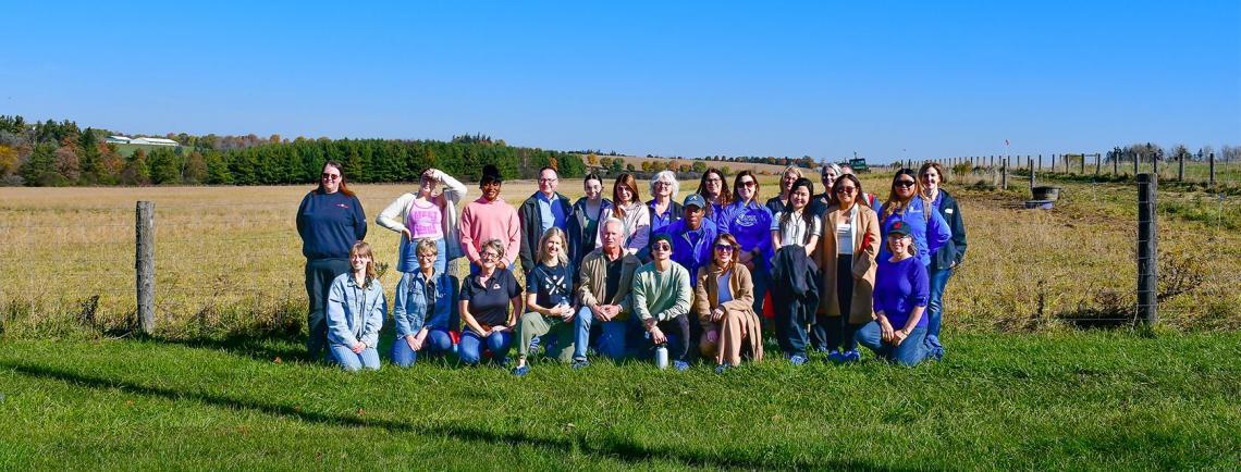 A group of about 20 people pose in front a field (pasture)