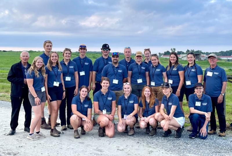 24 U of G students, dressed in matching shirts, and their professors post together outside under grey skies and near a green farm field