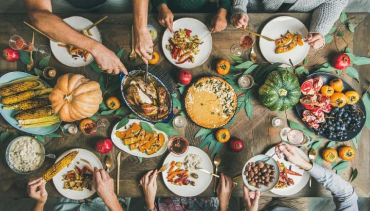 A top-down view of a table covered in fresh food, and hands of many friends reaching for the dishes.