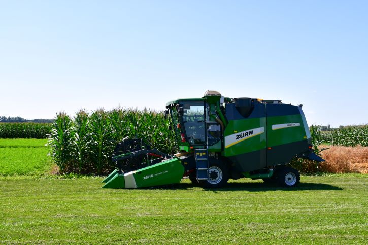 A new-looking combine machine stands higher than the tall wheat in the field directly behind it.