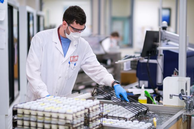 Raw milk in vials being mixed by a lab worker wearing a mask and eye protection