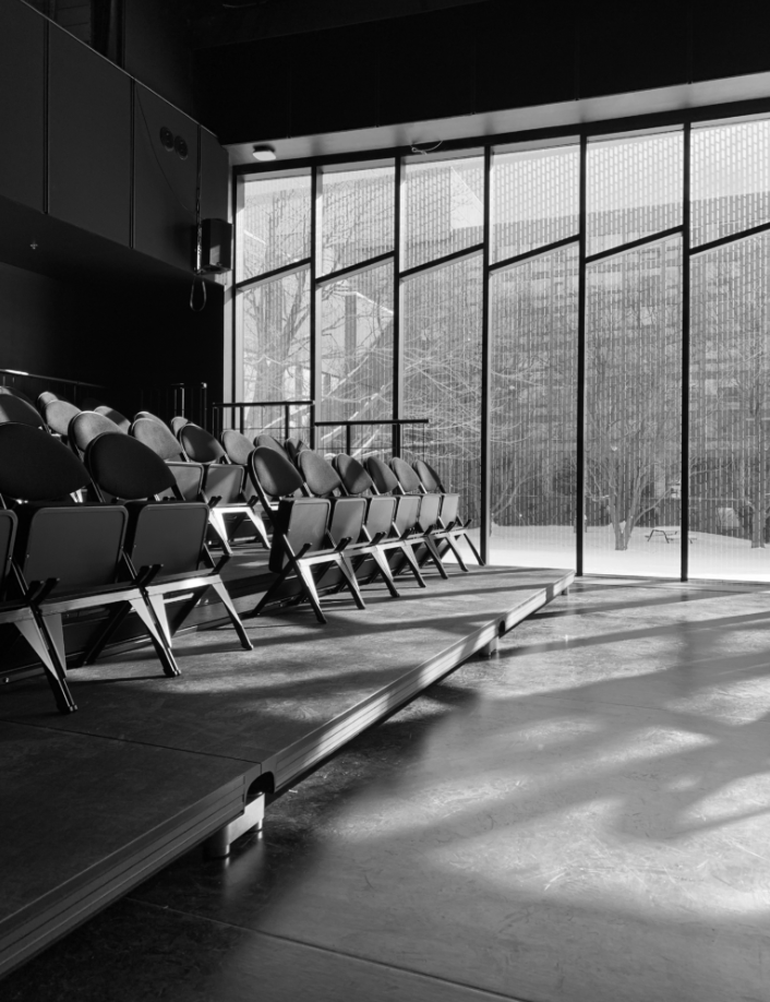 Black and white image of the improvisation lab located within the Arts Research Centre at the University of Guelph, featuring chairs arranged on the stage.