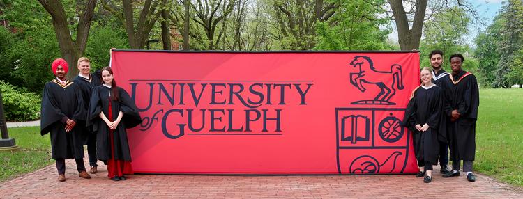University of Guelph students in graduation gowns holding a university banner