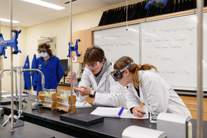 Two students working with lab equipment in a chemistry classroom.