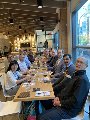 Group of symposium speakers sitting at a table gathered for dinner looking at the camera.