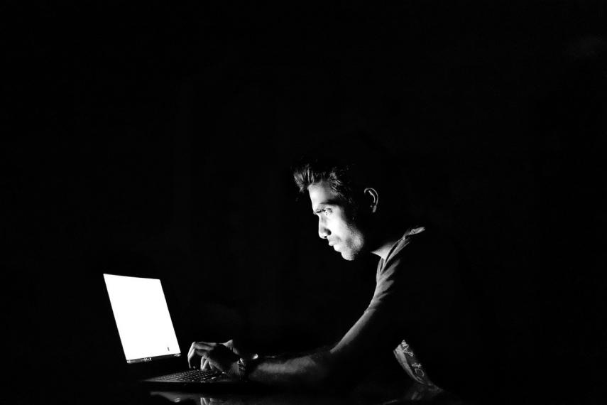 Image of person in dark looking at computer screen shrouded in mystery