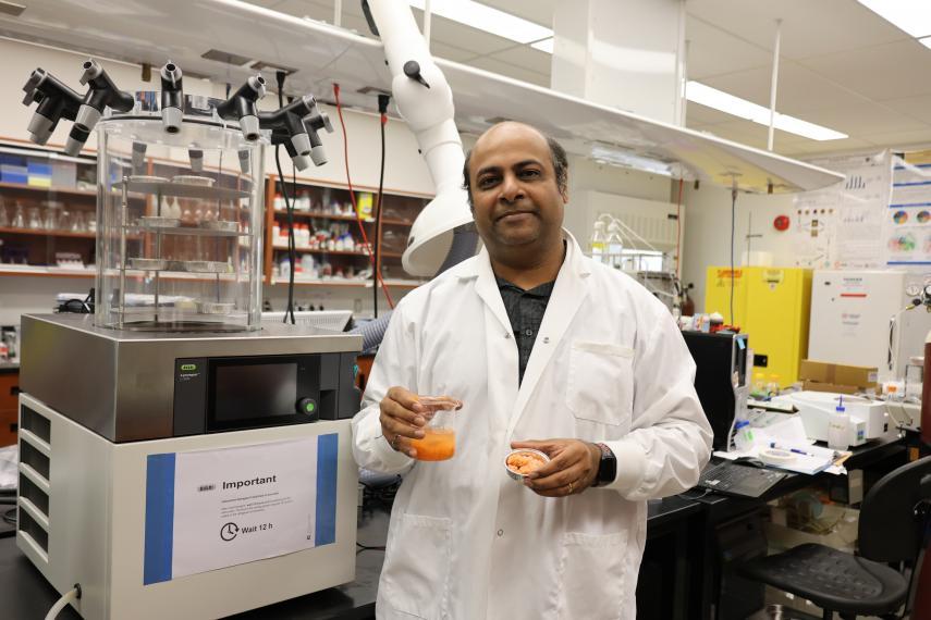 Dr. Ashutosh Singh standing in the lab holding a beaker of carrot juice and an aluminum tray of frozen carrot puree.