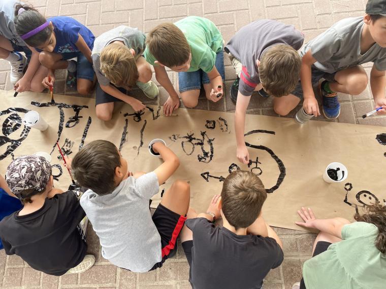 A group of campers in grades 2-3 paint a banner during a Creative Encounters Summer Camp