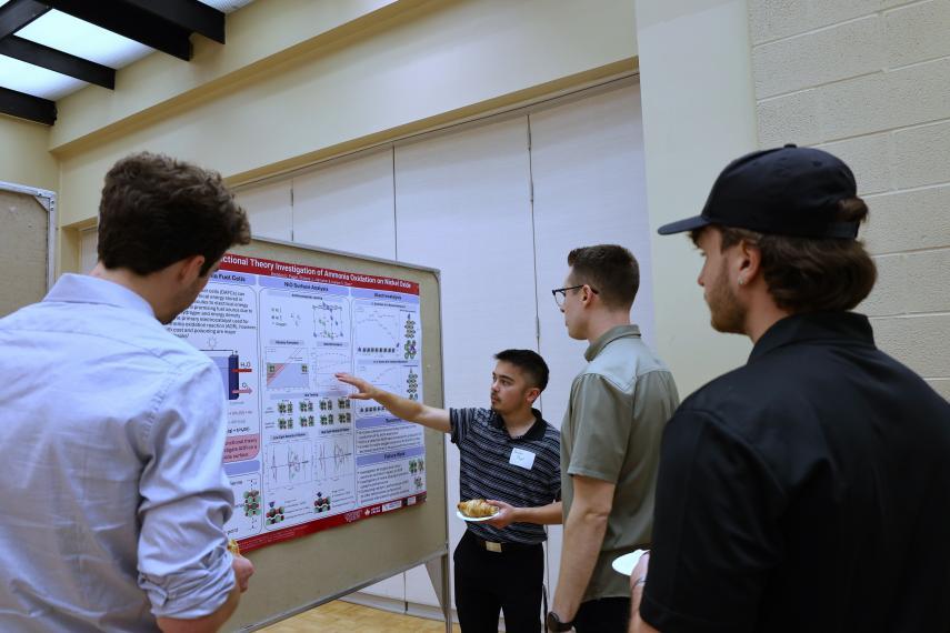 Student presenting their research poster while three other students listen.