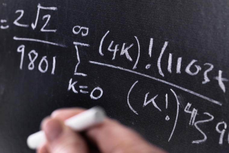 Whiteboard with equation and hand holding a piece of chalk. 