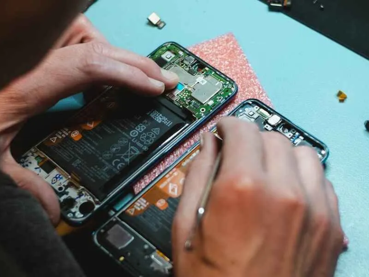 A pair of hands works on repairing the inside wiring of a phone laying on a table