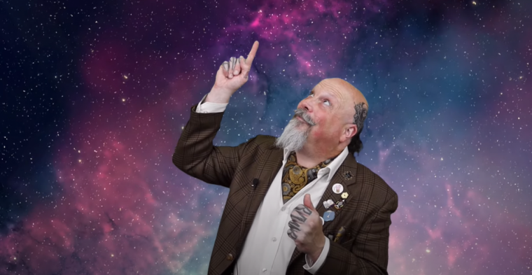 Orbax looking and pointing upward with a galaxy background behind him.