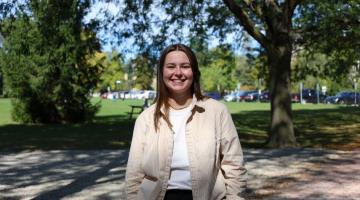 Aeryn Mac Isaac standing on Alumni Walk in front of trees near Johnston Green.