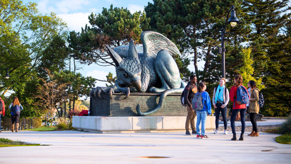 A group of five students talking beside the Gryphon statue at the University of Guelph