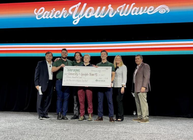 A group of people standing together holding a large cheque. 