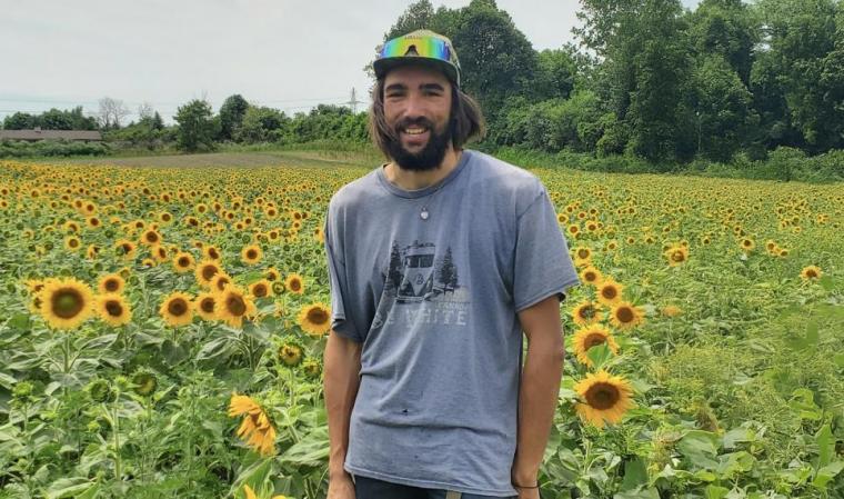 Mathew Hartman smiling with a field of sunflowers behind him. 