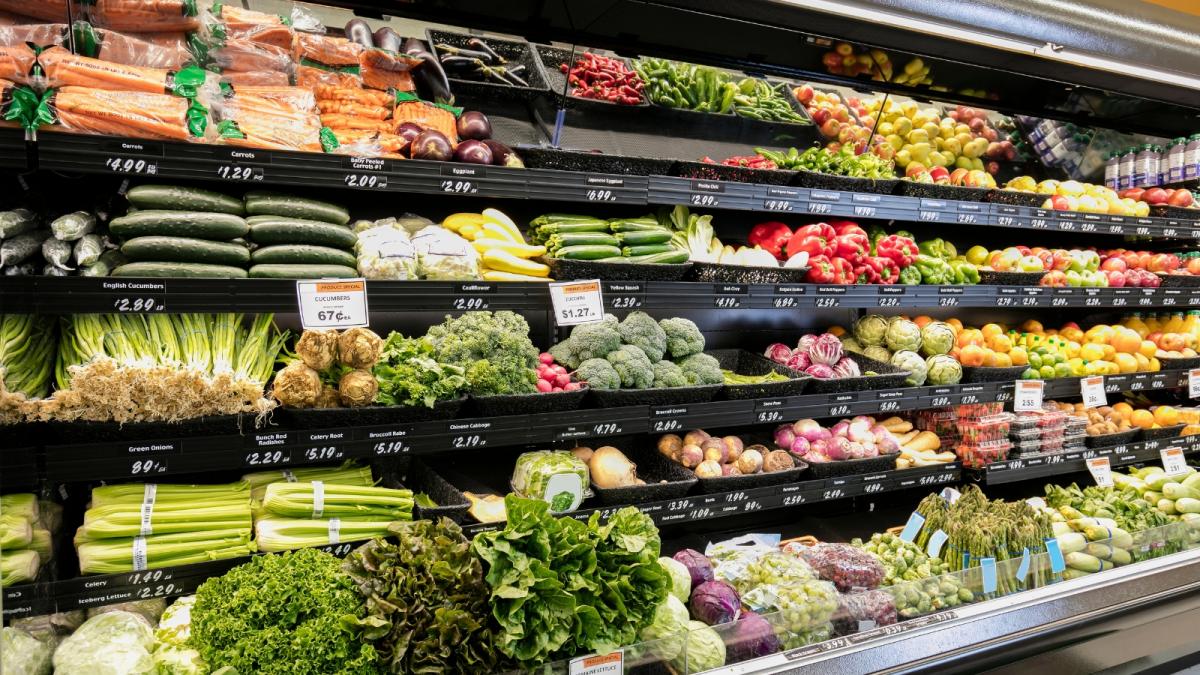 Produce cooler section in a grocery store filled with a variety of fresh vegetables.