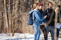 Students standing in a wooded area holding clip boards.