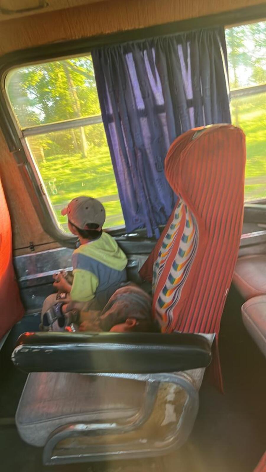 Two children riding on a bus. One is sitting up and looking out the window while the other is nestled beside him on the seat.