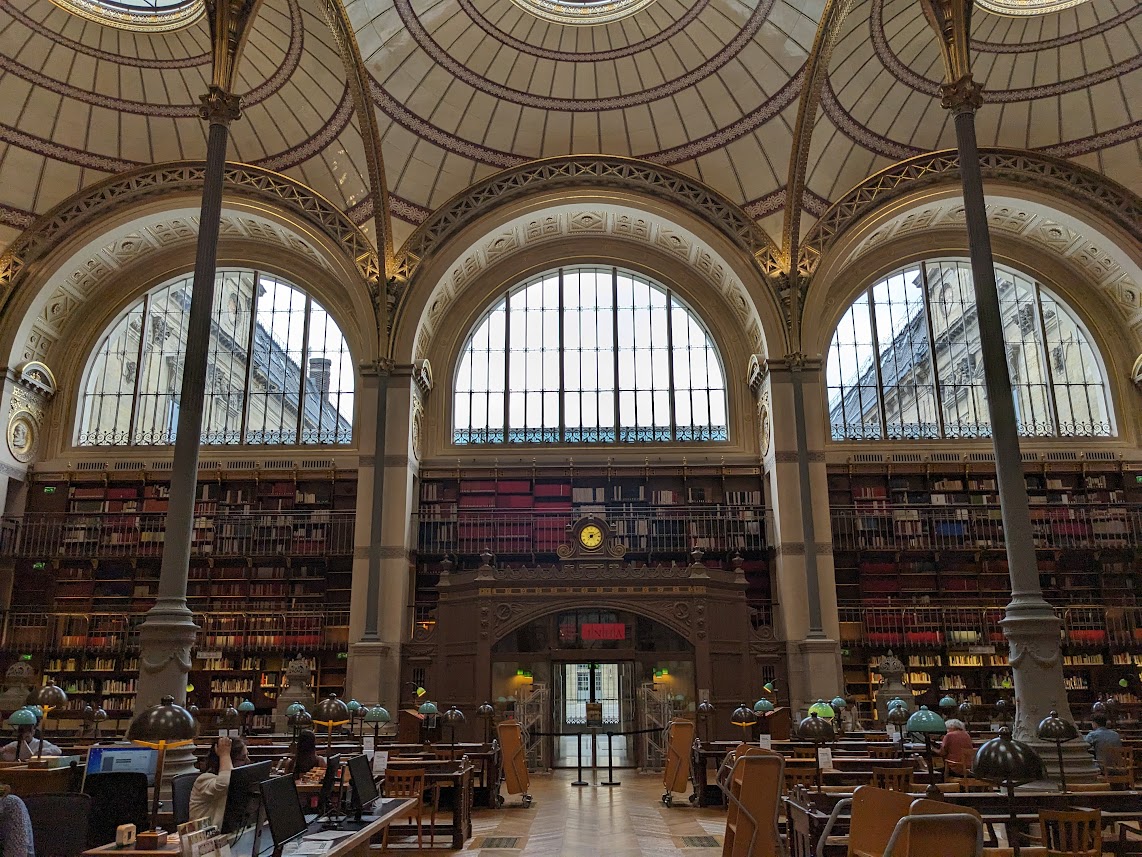 The inside of the French National Library with the high ceilings, arches and shelves of books with students sitting at computers on the main floor. 