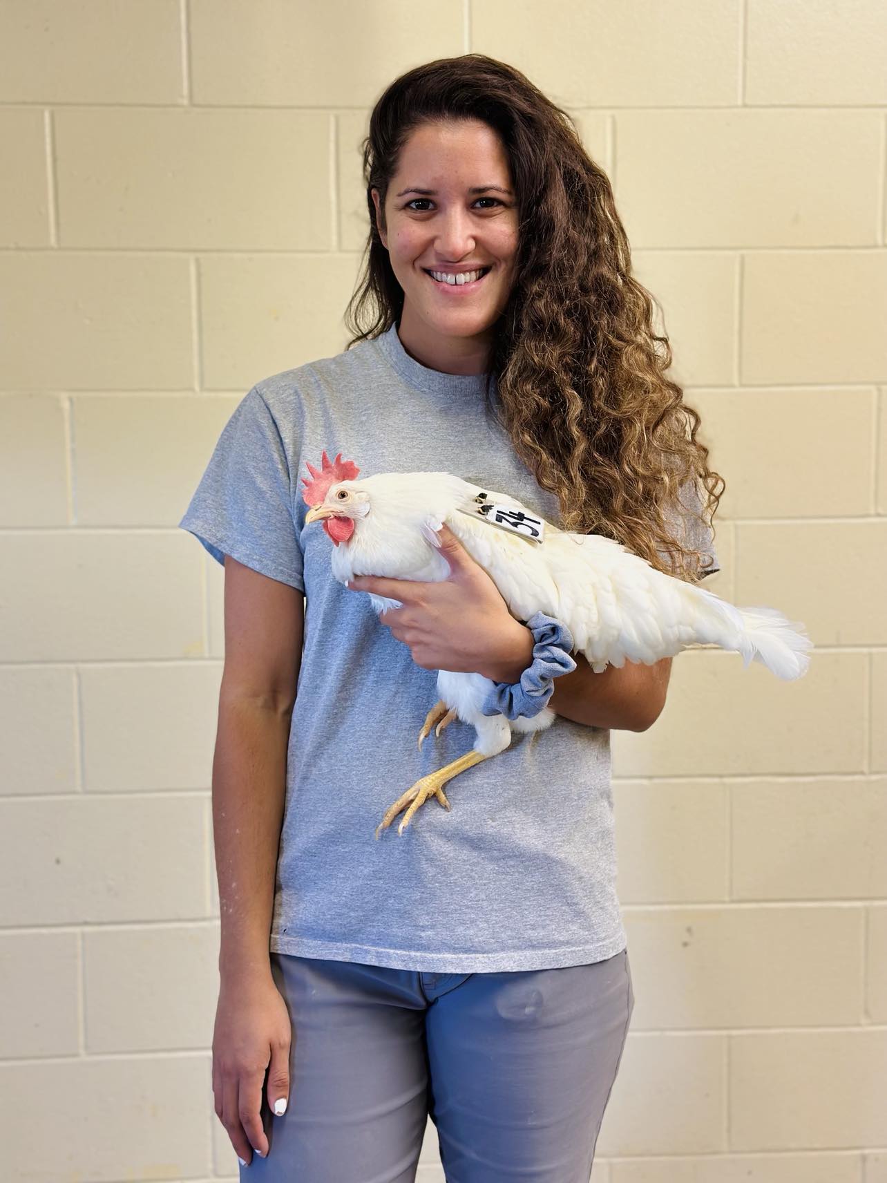  A woman with curling hair wearing a t-shirt and jeans holding a white chicken.