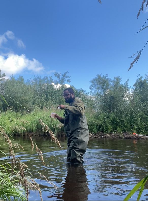 A man in water surrounded by tall grass using a drone