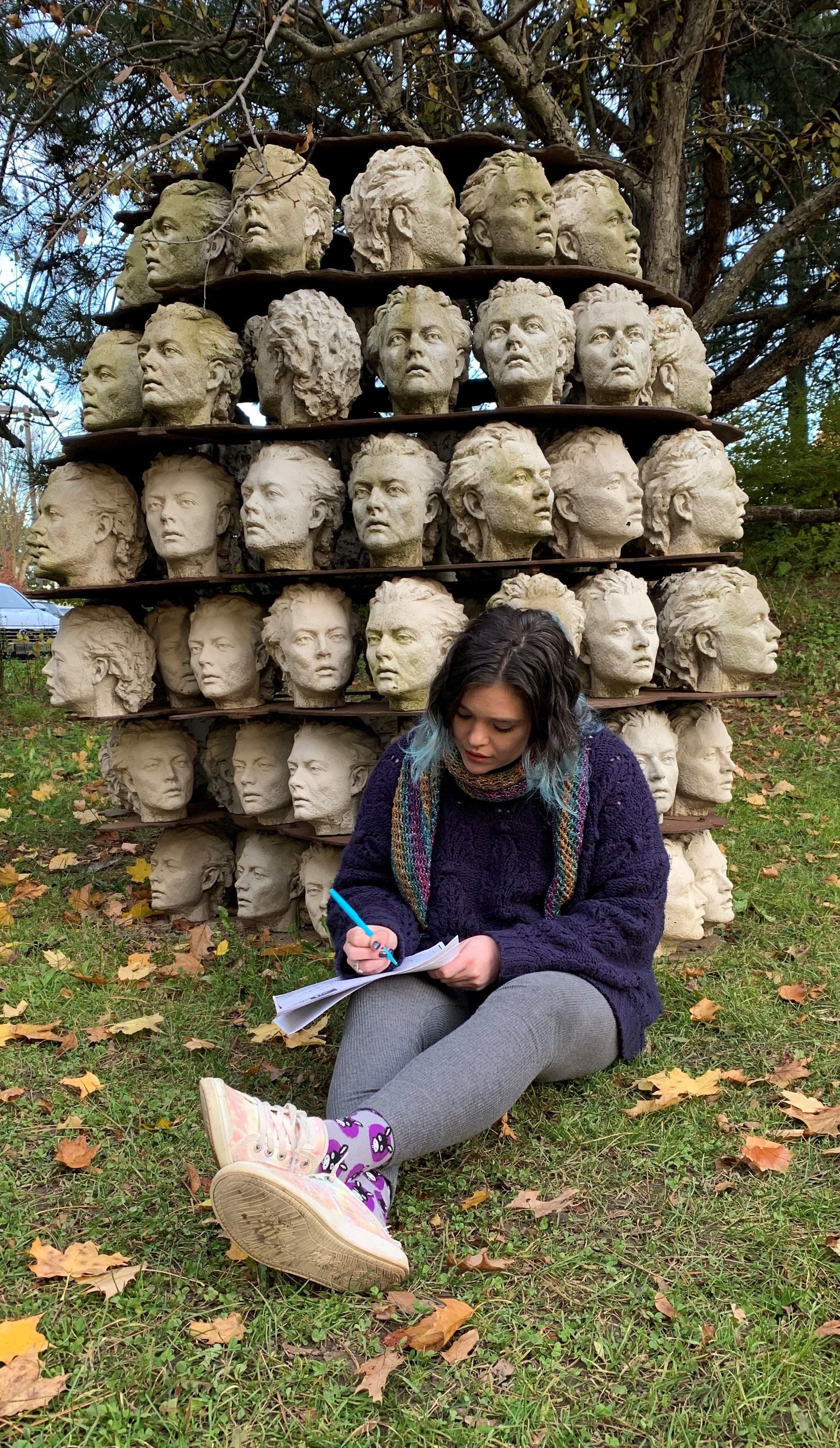 A woman sitting in the Donald Forster Sculpture Park in front of head sculptures