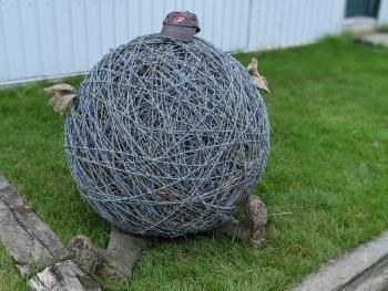 A ball of barbed wire sits with a hat, gloves, and boots sticking out from it 