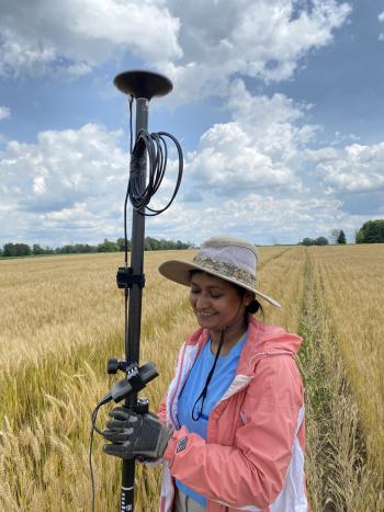A student standing in a wheat field and  trying to GPS her plots.