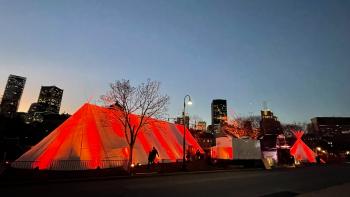 An Indigenous village in Montreal at night. There is a big tent and a teepee that are glowing red.