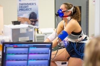 A woman on a bike wearing equipment to measure the amount of oxygen her body can use, her blood pressure and the amount of blood her heart is delivering to the active muscles during exercise