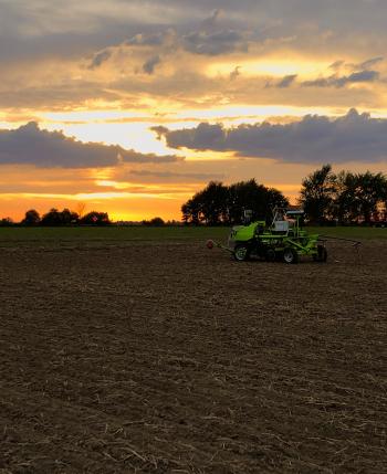 A robotic device on a barren wheat field at sunset.